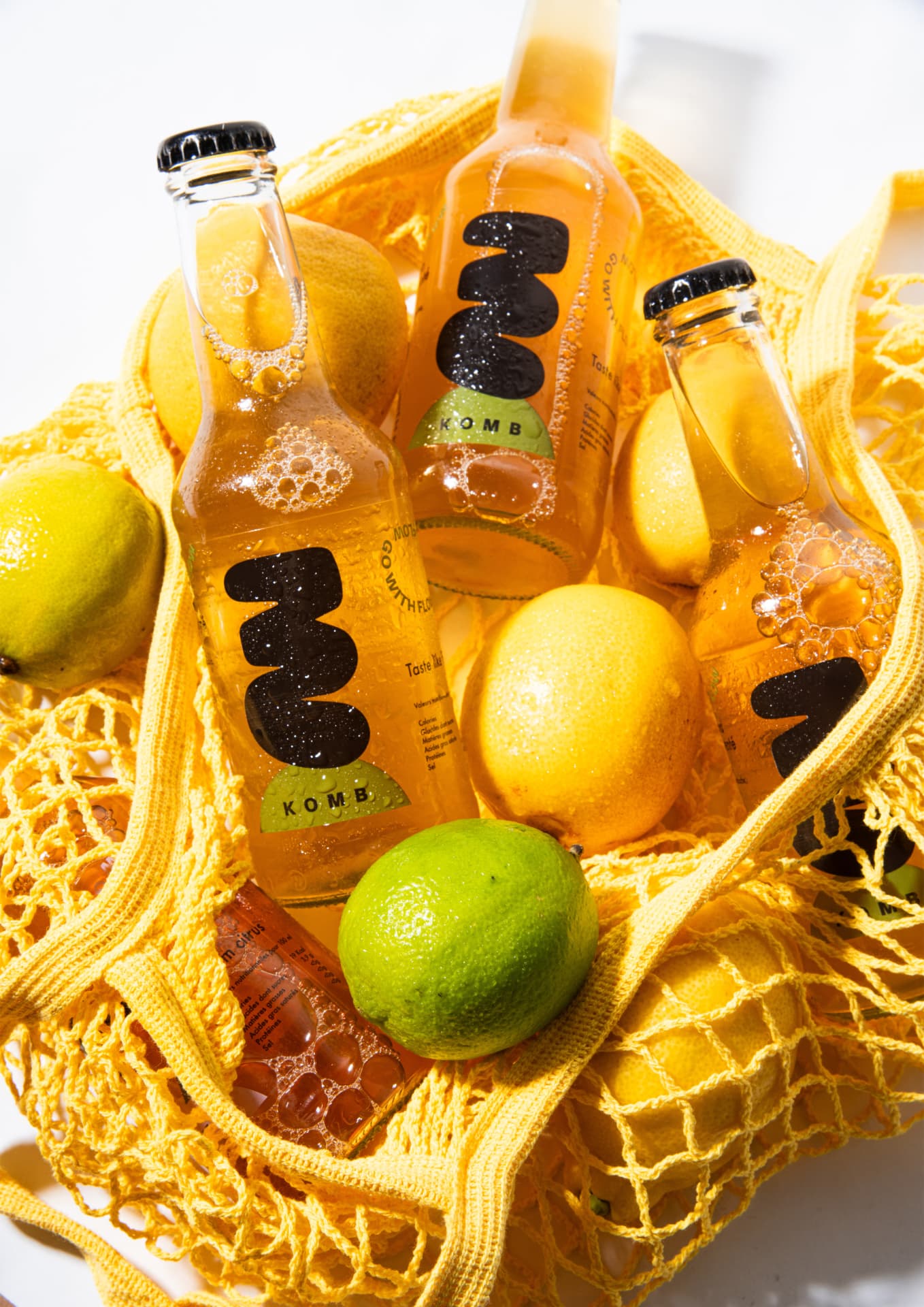 Bouteilles KOMB et agrumes dans un filet jaune, ambiance estivale